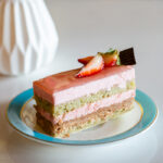 A plated slice of cake of strawberry Mousse layered with pistachio sponge cake